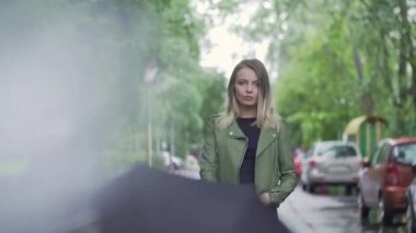 Genç Avrupalı bir kız elinde siyah bir şemsiyeyle duruyor.