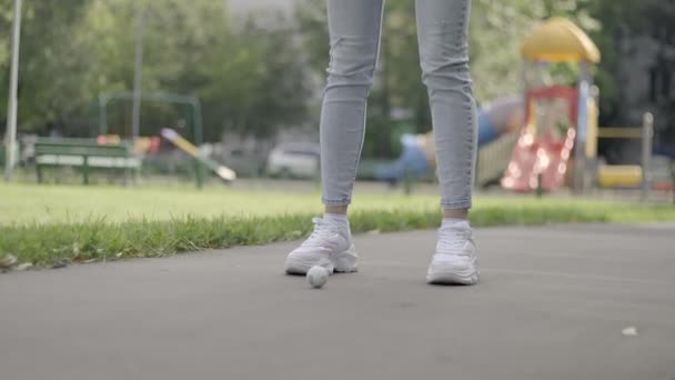 Pernas de uma jovem menina em tênis brancos estão batendo uma bola de golfe — Vídeo de Stock
