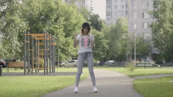 Молодая девушка в белых кроссовках бьет мячом для гольфа — стоковое видео