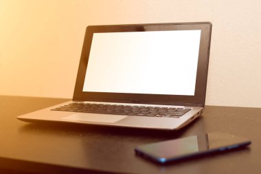 Koyu ahşap masada siyah cep telefonlu gümüş bir dizüstü bilgisayar.