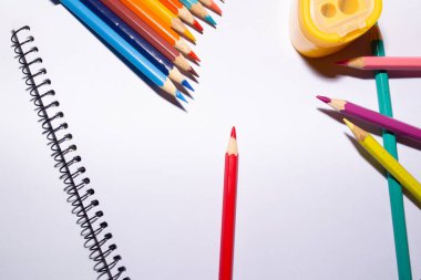 Bir çizim defteri, renkli kalemler ve beyaz arka planda bir keskinleştirici.