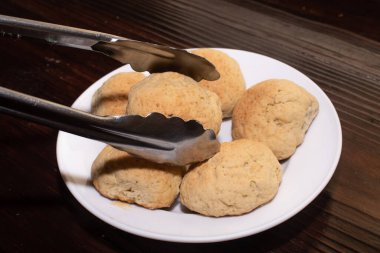 Ekmek rulosu tutan metal maşalar, beyaz tabakta bir grup ekmek rulosundan.