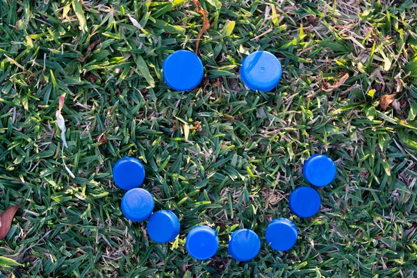 Plastic bottle caps on a grass background forming a happy face, recycling