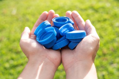 Geri dönüşüm, iki el plastik şişe kapağı, yeşil çimen arka planı