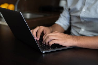 Adam elleri dizüstü bilgisayarda yazıyor, mutfakta oturuyor. Evde çalışıyorum.