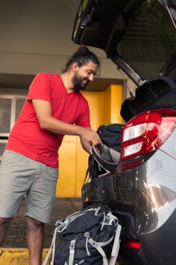 Arabanın bagajına bavul taşıyan bir adam yolculuğa çıkmaya hazır.