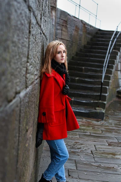 Vrouw in een rode jas leunend op een oude steen — Stockfoto