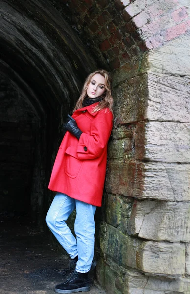 Woman wearing a red coat leaning against an old wall of a tunnel — Stock Photo, Image