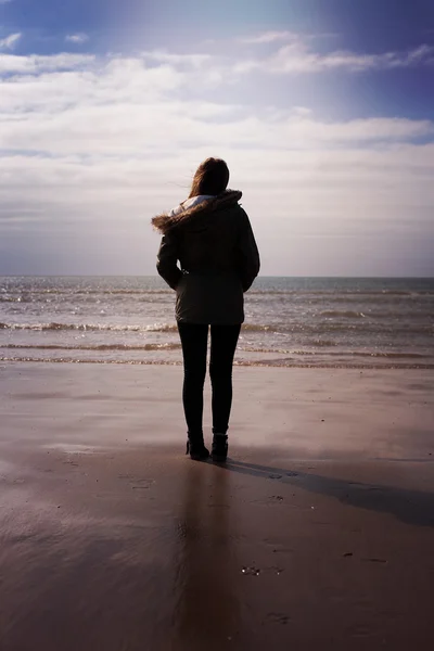 Achterzijde van een jonge vrouw aan het strand kijkt uit naar zee — Stockfoto