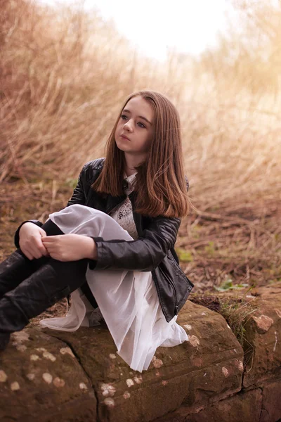 Menina adolescente bonita sentada em uma parede de pedra olhando para o — Fotografia de Stock