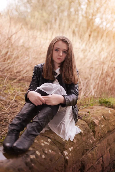 Beautiful teenage girl sitting on a stone wall looking s — стоковое фото