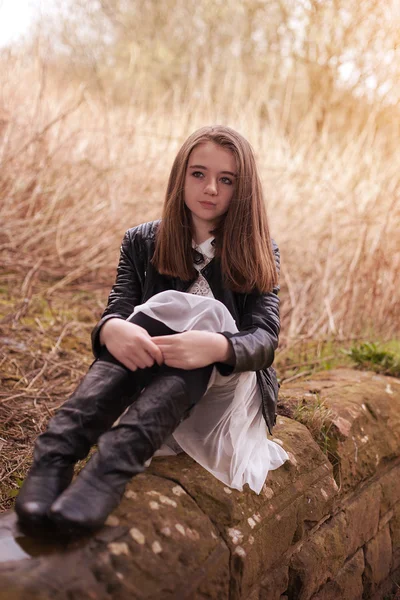 Hermosa adolescente sentada en una pared de piedra mirando dentro de la —  Fotos de Stock