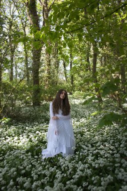 Uzun beyaz elbise ayakta çiçek bir halı üzerinde bir ormandaki güzel kadın
