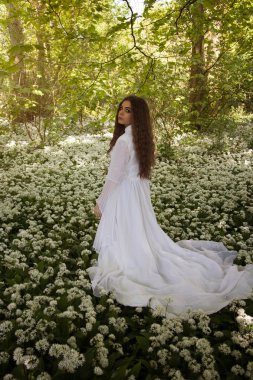 Bir ormanda ayakta beyaz uzun elbiseli güzel kadın