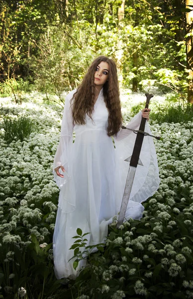 Mulher bonita usando um longo vestido branco segurando uma espada medieval — Fotografia de Stock