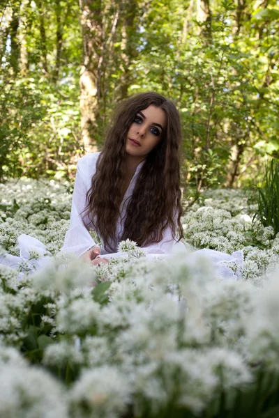 Bir ormanda oturan uzun beyaz bir elbise giyen güzel kadın — Stok fotoğraf