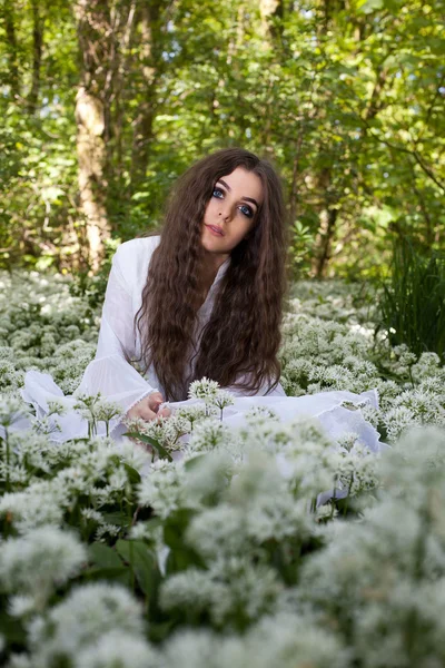 Hermosa mujer con un vestido largo y blanco sentada en un bosque — Foto de Stock