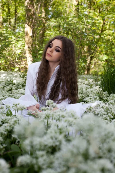 Krásná žena na sobě dlouhé bílé šaty sedí v lese — Stock fotografie