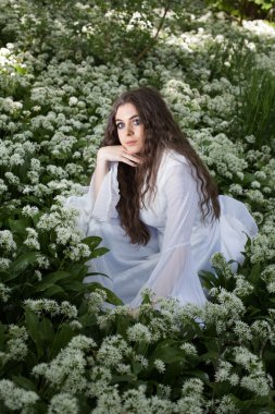 Beyaz çiçekler içinde oturan uzun beyaz bir elbise giyen güzel kadın