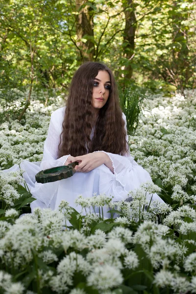 Beyaz çiçekler içinde oturan uzun beyaz bir elbise giyen güzel kadın — Stok fotoğraf