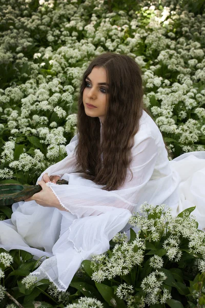 Hermosa mujer con un vestido blanco largo sentado en flores blancas —  Fotos de Stock