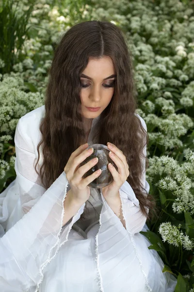 Hermosa joven en un bosque mirando una bola de cristal — Foto de Stock