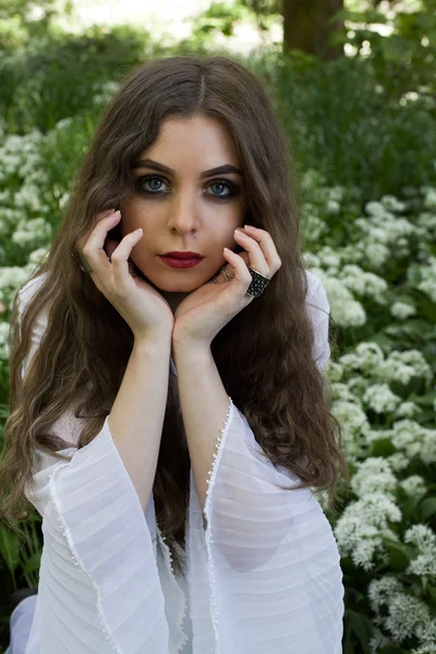 Piękna dziewczyna ubrana w długiej, białej sukni siedzi w białe kwiaty — Zdjęcie stockowe