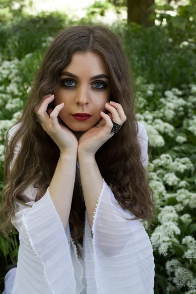 Beautiful woman wearing a long white dress sitting in white flowers — Stock Photo, Image