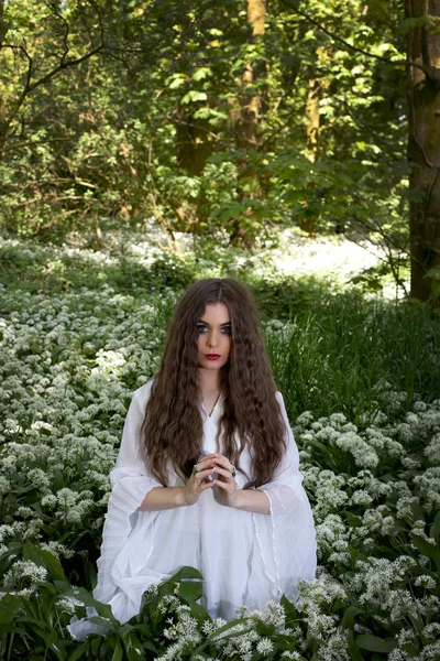 Beyaz çiçekler içinde oturan uzun beyaz bir elbise giyen güzel kadın
