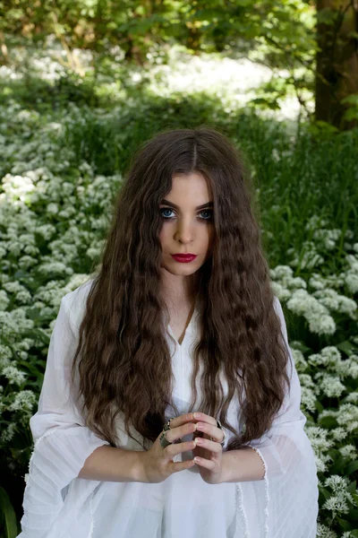 Beyaz çiçekler içinde oturan uzun beyaz bir elbise giyen güzel kadın