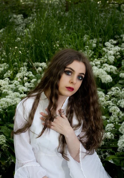 Hermosa mujer con un vestido blanco largo sentado en flores blancas —  Fotos de Stock