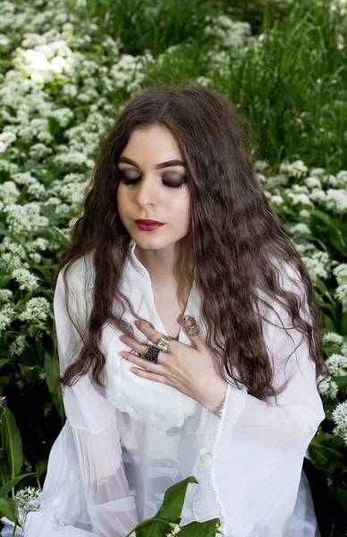 Mooie vrouw draagt een lange witte jurk zit in witte bloemen — Stockfoto