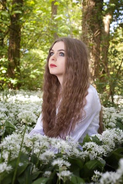 Piękna dziewczyna ubrana w długiej, białej sukni siedzi wśród białych kwiatów — Zdjęcie stockowe