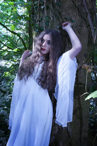 Hermosa mujer vistiendo un vestido blanco largo de pie contra un árbol —  Fotos de Stock