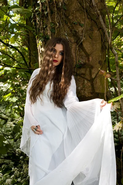 Hermosa mujer con un vestido blanco largo de pie contra un tr —  Fotos de Stock