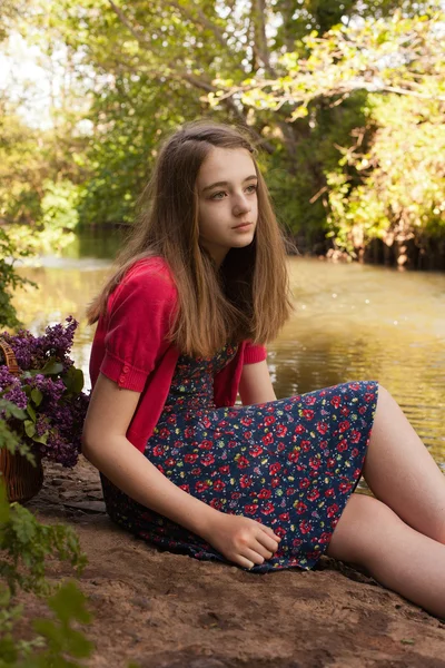 Schöne Teenager-Mädchen sitzt neben einem Fluss — Stockfoto