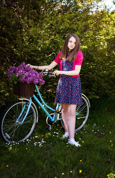 Beautiful teenage girl standing beside a bicycle with a basket of flowers — Stock Photo, Image