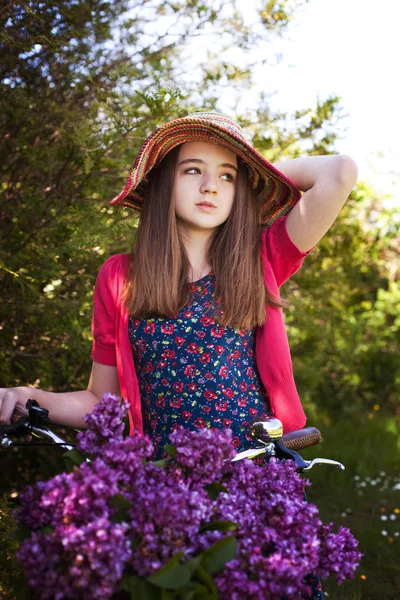 Beautiful teenage girl sitting on a bicycle with a basket of flowers — Stock Photo, Image