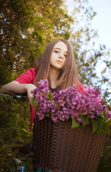 Beautiful teenage girl sitting on a bicycle with a basket of flowers — Stock Photo, Image