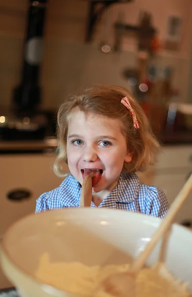 Young girl who has been baking liking the spoon.