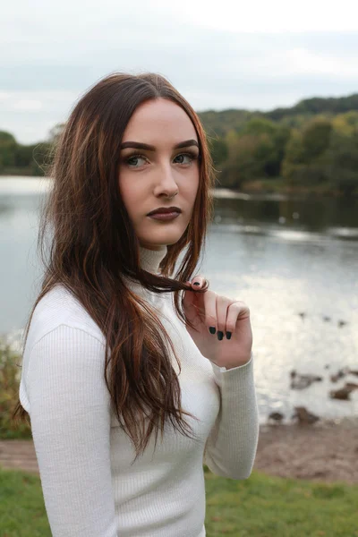 Mulher bonita em um parque com lago no fundo — Fotografia de Stock