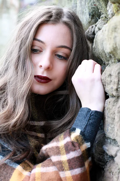 Schöne junge Frau mit einem Schal, der sich an einen Stein lehnt — Stockfoto