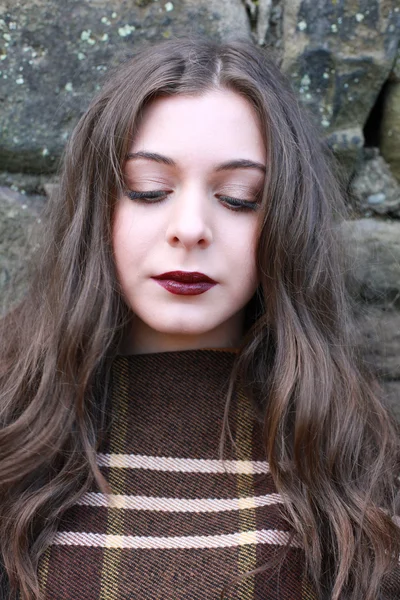 Beautiful young woman leaning on a stone wall with eyes cast dow — Stock Photo, Image