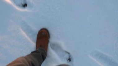 Karlı bir kış akşamında kar manzaralı bir yerde yürüyen bir adamın ayakları..