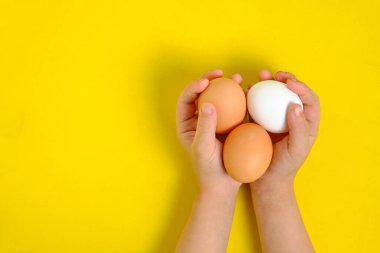 Sarı arka plandaki bir çocuğun ellerinde üç tavuk yumurtası.