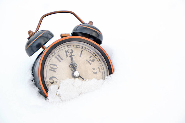 Old retro alarm clock in winter in snow on white background shows twelve hours