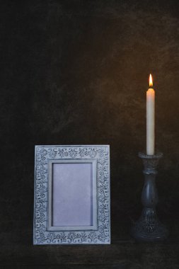 Eski bir fotoğraf çerçevesi, eski bir ahşap masanın üzerinde duran eski bir şamdanla yakılır.