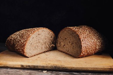 Two halves of sliced bread sprinkled with sesame seeds on a wooden cutting board