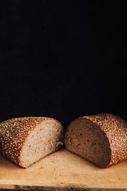 Two halves of sliced bread sprinkled with sesame seeds on a wooden cutting board