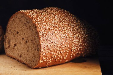 Koyu arkaplanda kesme tahtasına susam tohumları serpiştirilmiş çörek.